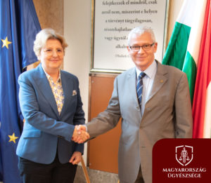 A fotón a szerb legfőbb ügyész asszony és a magyar legfőbb ügyész kezet fognak, a magyar és az uniós zászló előtt.
