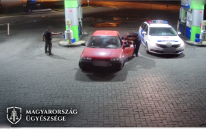 Képrészlet a videóból, ahogy egy férfi elsodorja a benzinkúton a rendőrt és a polgárőrt autójával